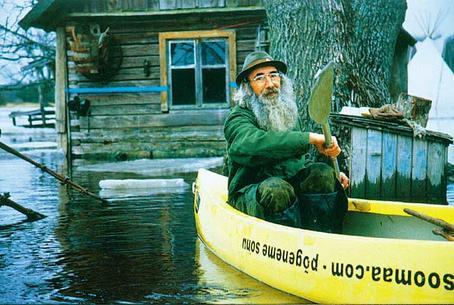 Soomaa.jpg: Aleksei Linnik liigub õue mööda ikka kanuuga. Sauna seinal tähistab sinine triip vee kõrgeimat teadaolevat taset, kuudi seinale löödud pulgake märgistab 2002. aasta kevadet.